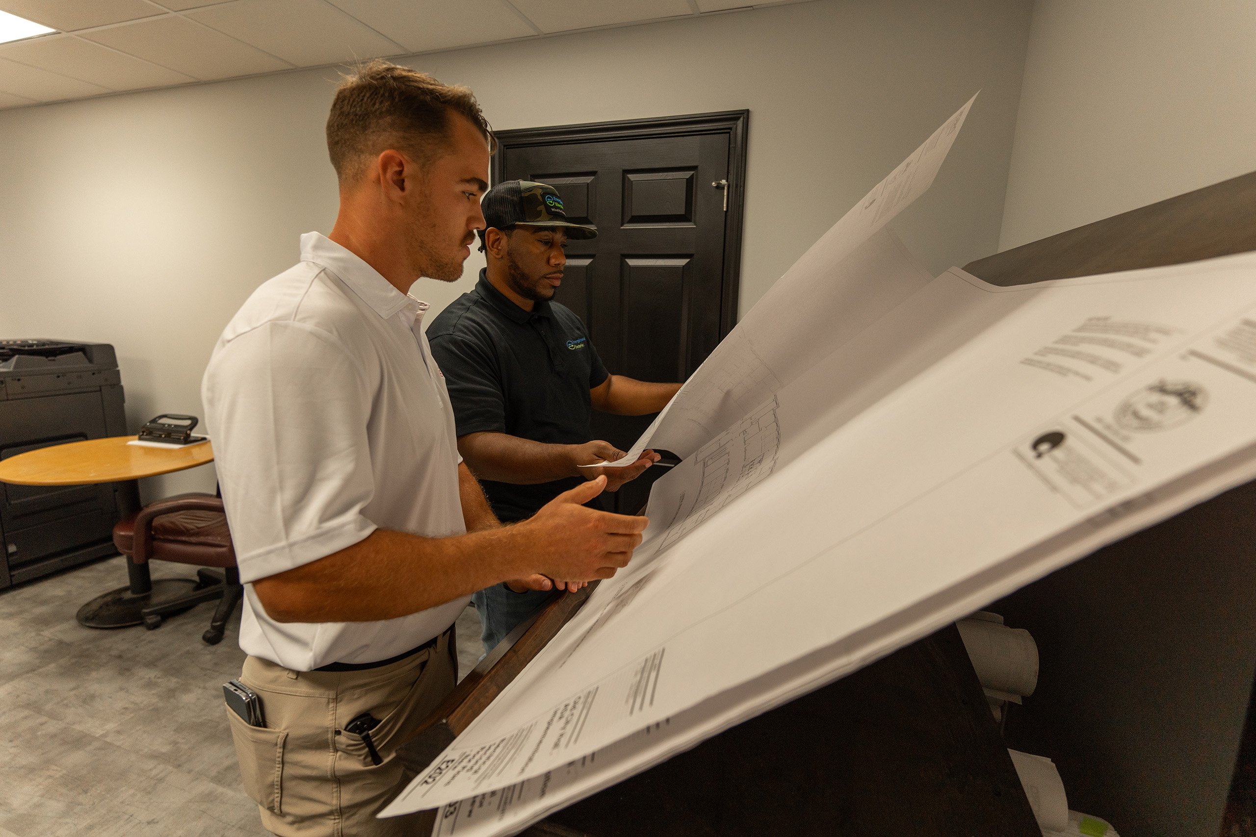 Construction professionals examining large-format building plans together Construction professionals examining large-format building plans together